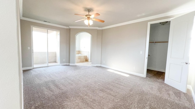 unfurnished bedroom featuring light carpet, crown molding, a walk in closet, and ensuite bath