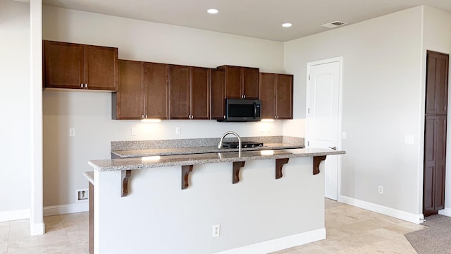 kitchen with light stone countertops, a kitchen breakfast bar, and a center island with sink