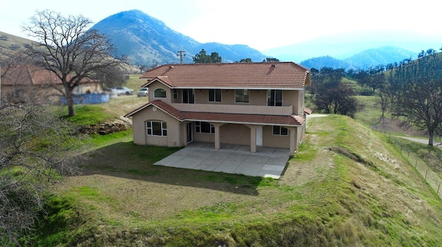 back of property with a mountain view, a lawn, and a patio