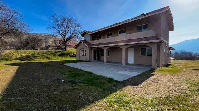 rear view of property with a mountain view, a yard, and a patio area