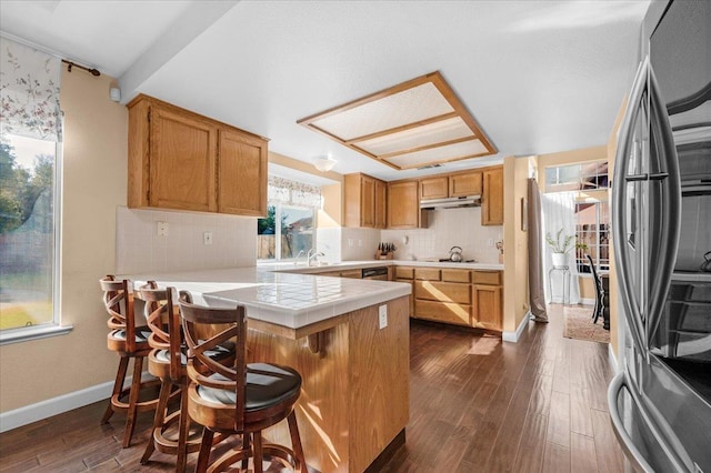 kitchen with stainless steel refrigerator, a kitchen breakfast bar, dark hardwood / wood-style floors, tasteful backsplash, and tile countertops