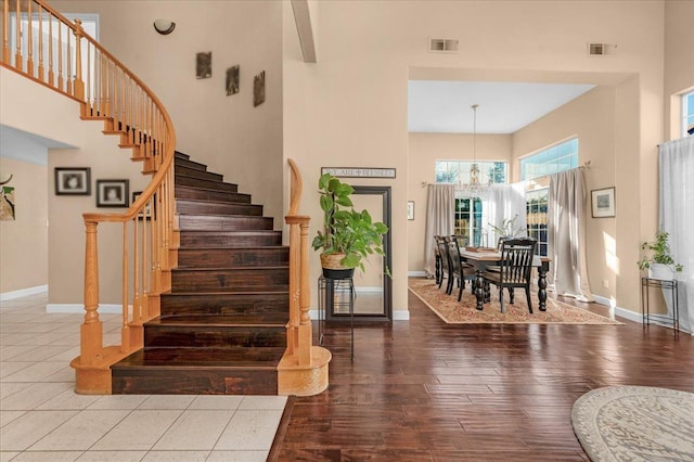 stairs with a towering ceiling, hardwood / wood-style floors, and a notable chandelier