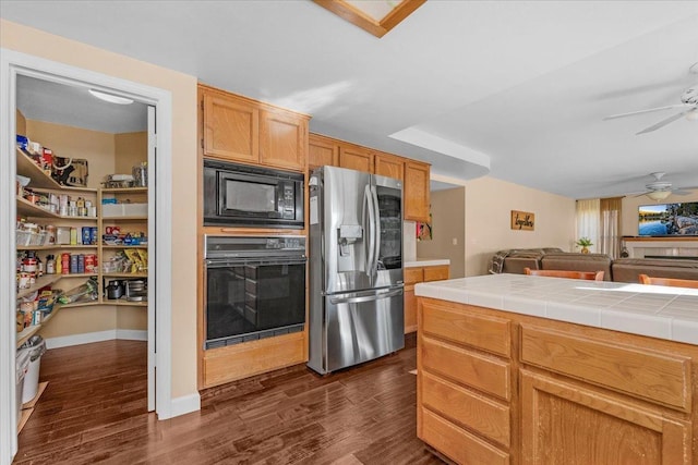 kitchen featuring dark hardwood / wood-style floors, ceiling fan, tile counters, and black appliances