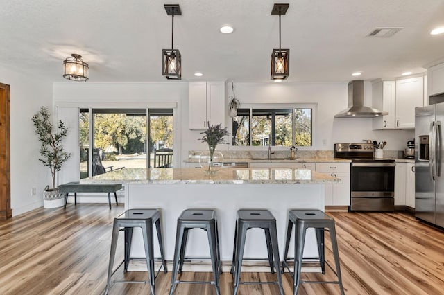 kitchen with pendant lighting, appliances with stainless steel finishes, wall chimney exhaust hood, and white cabinets