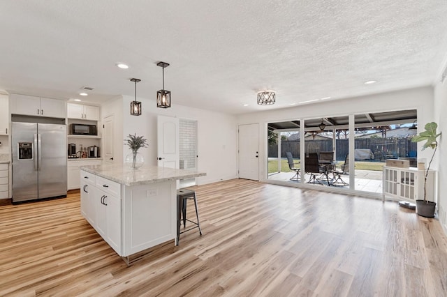 kitchen featuring decorative light fixtures, built in microwave, white cabinets, stainless steel fridge, and a center island