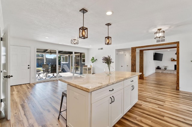 kitchen with a kitchen island, pendant lighting, white cabinets, light stone countertops, and light hardwood / wood-style flooring