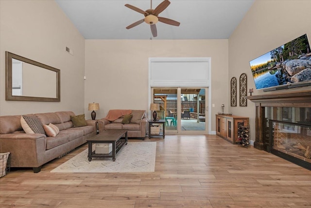 living room featuring a high ceiling, ceiling fan, and light wood-type flooring