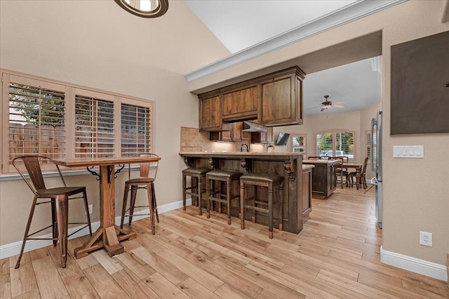 kitchen featuring a kitchen bar, stainless steel fridge, kitchen peninsula, ceiling fan, and light hardwood / wood-style floors