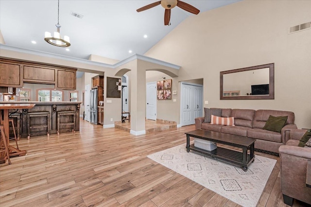 living room featuring ceiling fan with notable chandelier, light hardwood / wood-style flooring, and high vaulted ceiling