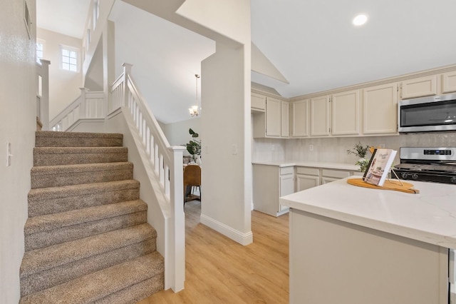 kitchen with pendant lighting, decorative backsplash, stainless steel appliances, cream cabinets, and light wood-type flooring