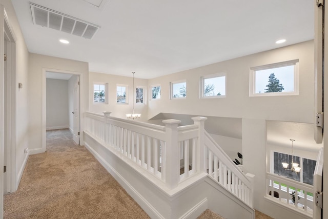 hallway with light carpet and a notable chandelier