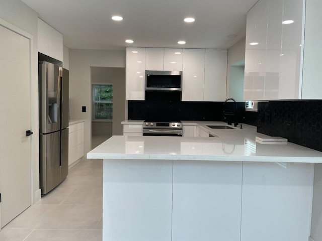 kitchen featuring sink, white cabinetry, stainless steel appliances, light stone counters, and kitchen peninsula