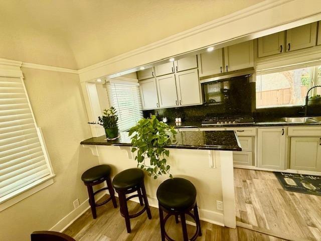 kitchen with stainless steel gas stovetop, sink, a kitchen bar, and light wood-type flooring