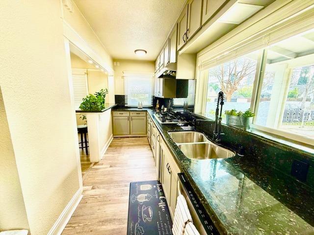 kitchen with sink, light hardwood / wood-style flooring, light brown cabinets, stainless steel gas stovetop, and dark stone counters