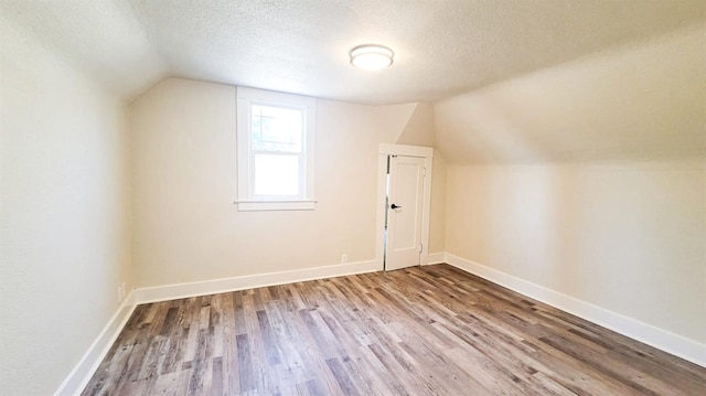 additional living space featuring wood-type flooring, a textured ceiling, and vaulted ceiling