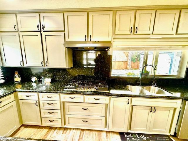 kitchen with sink, dark stone countertops, backsplash, stainless steel gas stovetop, and light wood-type flooring