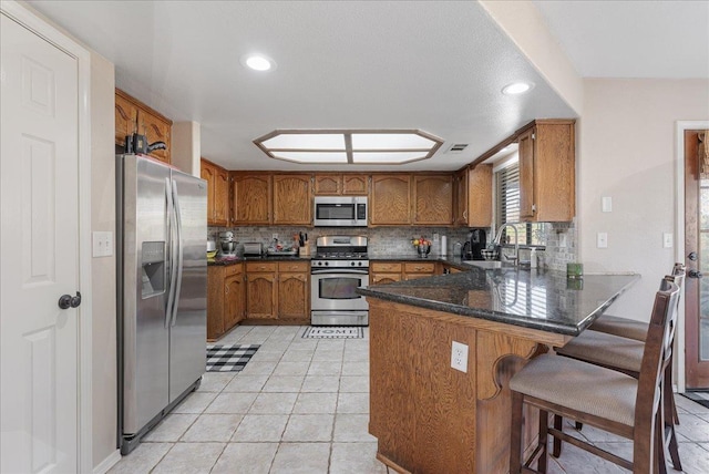 kitchen with sink, appliances with stainless steel finishes, backsplash, a kitchen breakfast bar, and kitchen peninsula