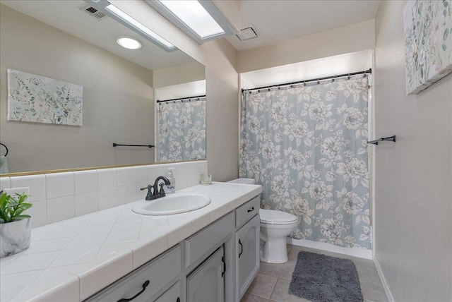 bathroom featuring vanity, toilet, a skylight, and tile patterned flooring