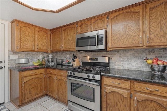 kitchen with tasteful backsplash, stainless steel appliances, dark stone countertops, and light tile patterned floors