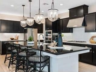 kitchen featuring a breakfast bar, a center island with sink, stainless steel refrigerator, pendant lighting, and black gas stovetop