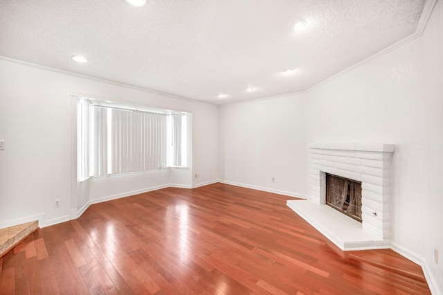 unfurnished living room featuring wood-type flooring, a brick fireplace, ornamental molding, and a textured ceiling