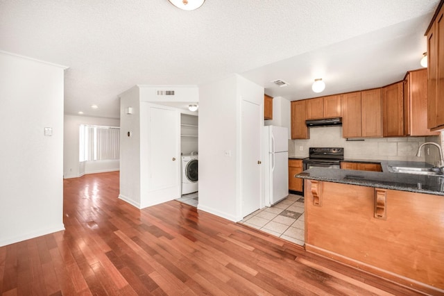 kitchen with black electric range oven, sink, light hardwood / wood-style flooring, white refrigerator, and washer / clothes dryer