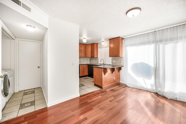 kitchen featuring a kitchen bar, a textured ceiling, light hardwood / wood-style flooring, dishwasher, and washer and clothes dryer