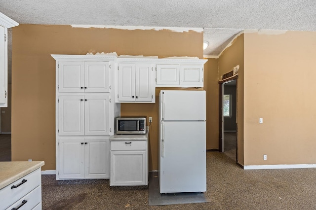 kitchen with white refrigerator, white cabinetry, and a textured ceiling