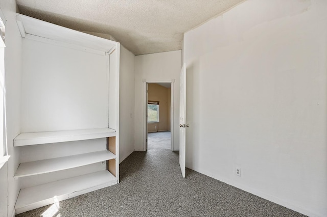 hall featuring a textured ceiling and dark colored carpet