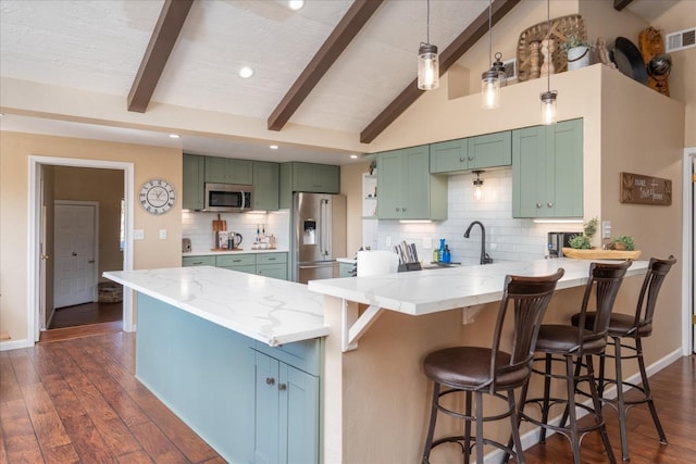 kitchen featuring a breakfast bar, light stone counters, green cabinetry, lofted ceiling with beams, and stainless steel appliances