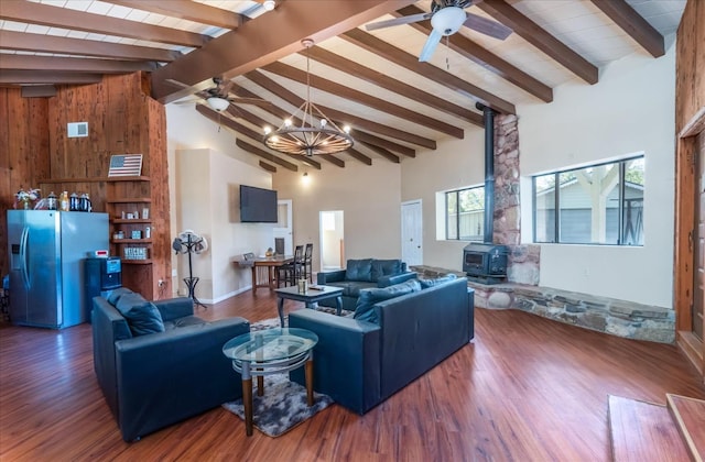 living room with ceiling fan with notable chandelier, high vaulted ceiling, wood-type flooring, a wood stove, and beam ceiling