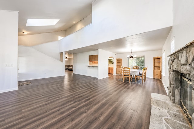 living room featuring an inviting chandelier, a towering ceiling, a skylight, dark hardwood / wood-style flooring, and a stone fireplace