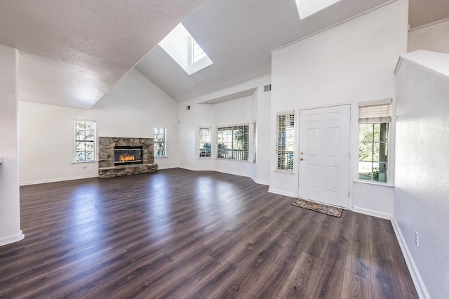 unfurnished living room featuring plenty of natural light, dark hardwood / wood-style floors, a stone fireplace, and high vaulted ceiling