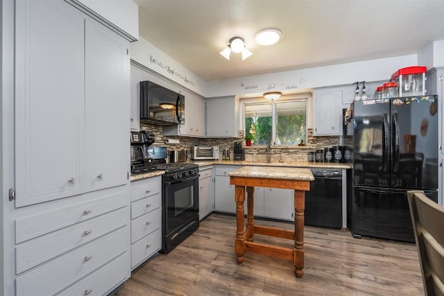 kitchen with sink, gray cabinetry, black appliances, hardwood / wood-style flooring, and backsplash