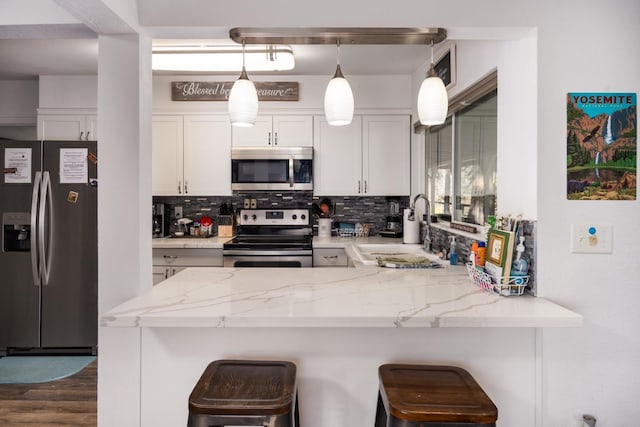 kitchen featuring a breakfast bar area, hanging light fixtures, appliances with stainless steel finishes, kitchen peninsula, and white cabinets