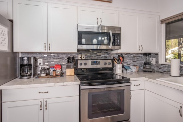 kitchen with tasteful backsplash, white cabinets, and appliances with stainless steel finishes