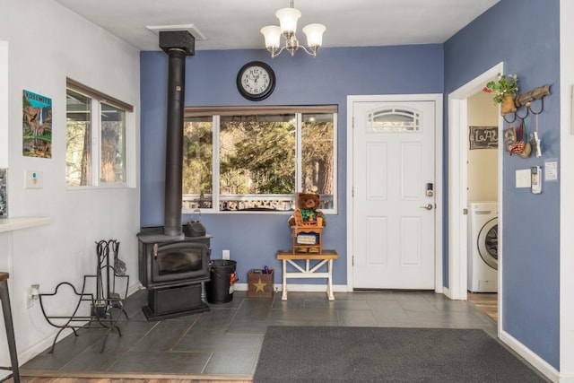 entryway with an inviting chandelier, washer / clothes dryer, dark tile patterned flooring, and a wood stove