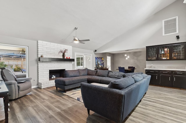 living room with ceiling fan, light wood-type flooring, bar, and a fireplace