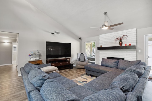 living room with hardwood / wood-style flooring, ceiling fan, high vaulted ceiling, and a brick fireplace