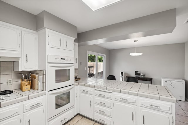 kitchen featuring white cabinetry, double oven, backsplash, tile countertops, and kitchen peninsula