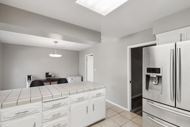 kitchen with light tile patterned flooring, decorative light fixtures, white cabinetry, tile counters, and stainless steel refrigerator with ice dispenser