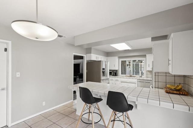 kitchen with a kitchen bar, light tile patterned floors, tile counters, stainless steel appliances, and white cabinets