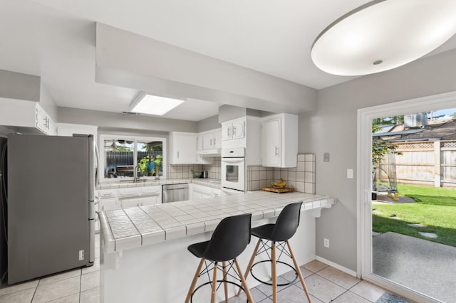 kitchen featuring light tile patterned floors, appliances with stainless steel finishes, white cabinets, tile countertops, and kitchen peninsula