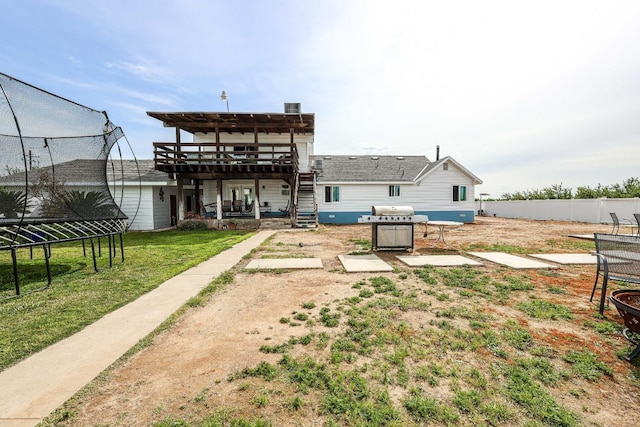 back of house featuring a patio, a lawn, a wooden deck, a trampoline, and a pergola