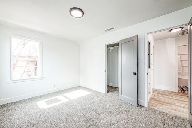 unfurnished bedroom with a closet, a spacious closet, and light carpet