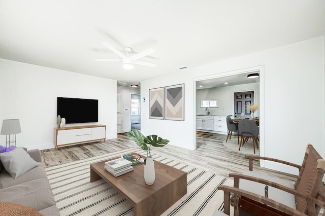 living room with ceiling fan, sink, and light wood-type flooring