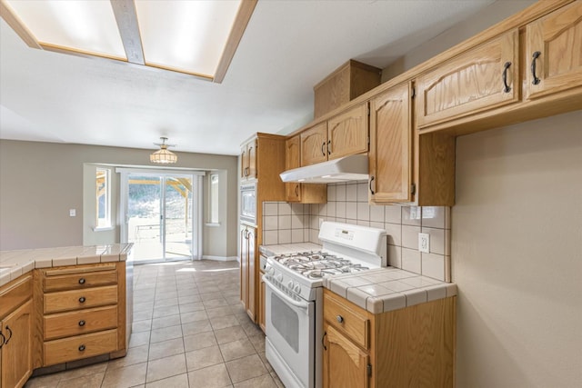 kitchen with tile counters, backsplash, white appliances, and light tile patterned floors