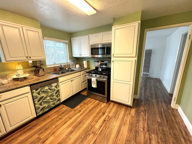 kitchen with sink, hardwood / wood-style flooring, white cabinetry, stainless steel appliances, and a textured ceiling