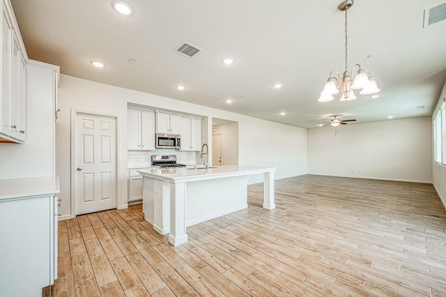 kitchen featuring appliances with stainless steel finishes, tasteful backsplash, white cabinets, a kitchen island with sink, and light hardwood / wood-style flooring