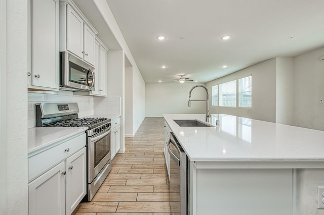 kitchen featuring sink, stainless steel appliances, white cabinets, and a center island with sink